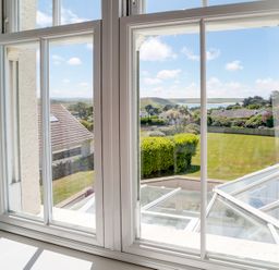 A view through a white framed window of a garden with trimmed hedges and houses beyond at The Haven in Daymer Bay