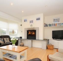 A living room with a fireplace a television a bookshelf and seating at Pendaveli in Polzeath