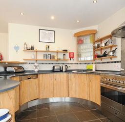 A kitchen with wooden cabinets black countertops stainless steel oven and open shelves at Pendaveli in Polzeath