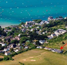 An aerial view of a coastal village with houses near the shoreline and boats in the water at Penny Liggan in Rock