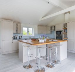 A kitchen with a wooden island countertop and three bar stools at Penny Liggan in Rock