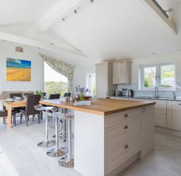 A kitchen with an island and stools next to a dining table with chairs and windows at Penny Liggan in Rock