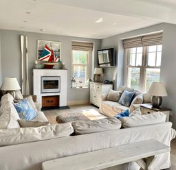 A living room with beige sofas blue cushions a fireplace and a television at Westray House in Polzeath