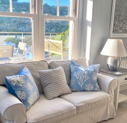 A living room with a white sofa with three cushions next to a side table with a lamp at Westray House in Polzeath