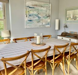A dining room with a large table covered by a striped tablecloth surrounded by eight wooden chairs at Westray House in Polzeath