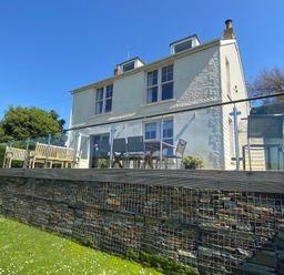 The exterior of a two story white house with a glass railing balcony and outdoor seating at Westray House in Polzeath