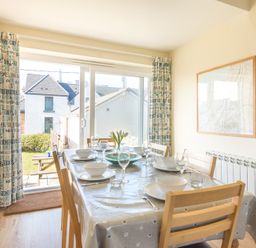A dining room with a table set for six near sliding glass doors with curtains at The Holiday House 2 Atlantic Mews in Polzeath