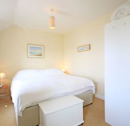 A bedroom with a white bedspread two lamps a chest and framed pictures on the wall at The Holiday House 2 Atlantic Mews Polzeath