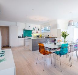 A modern kitchen and dining area with colorful chairs and a dining table set for a meal at Stepper Point in Polzeath