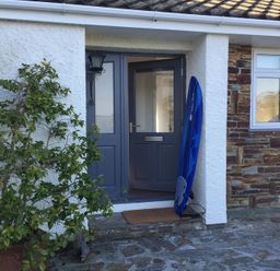 A front door with a blue surfboard leaning against the wall and a potted plant beside it at Corriana in Rock