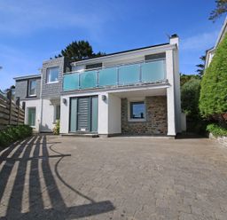 A modern two story house with a paved driveway a glass balcony and surrounding trees at Drifters Rock