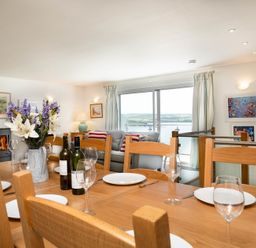 A dining table set with plates wine glasses and flower vase near a living room with sofa and large window showing a water view at Drifters in Rock