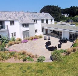A patio area with outdoor seating and plants around a white two story house at Downalong in Daymer Bay