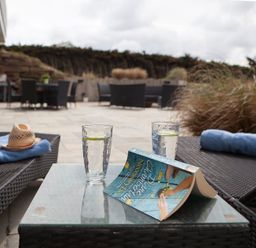 An outdoor patio with two lounge chairs a glass table with two glasses of water and a book at Downalong Daymer Bay