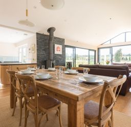 A dining table set with plates bowls and glasses in an open plan kitchen and living area with large windows at Chy-An-Dowr in Rock