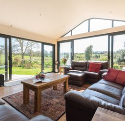 A living room with leather sofas a wooden coffee table and large glass windows overlooking a garden at Chy-An-Dowr in Rock