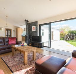 A living room with brown leather sofas a wooden coffee table and large sliding glass doors opening to a garden at Chy-An-Dowr in Rock