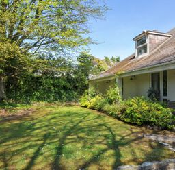 A yard with grass and a tree next to a house with plants along the side at Sandy Lodge Rock in Rock