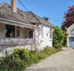 An exterior view of a white house with a gravel driveway and detached garage at Sandy Lodge Rock