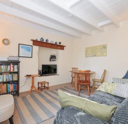 A living room with a sofa and bookshelf at Coppingers Cottage in Polzeath