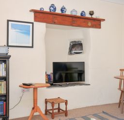 A living room with a bookshelf, television, and table at Coppingers Cottage, Polzeath