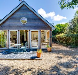 A small wooden house with glass doors and patio furniture outside at Greystones Studio in Daymer Bay