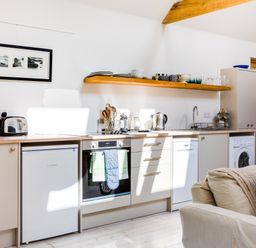 A kitchen with appliances cabinets and a wooden shelf with dishes at Greystones Studio in Daymer Bay