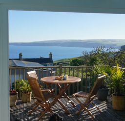 A wooden patio table and chairs with plants on a balcony overlooking the sea at The Porthole in Port Isaac