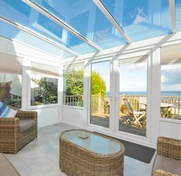 A conservatory with wicker furniture and a view of the sea at The Porthole in Port Isaac