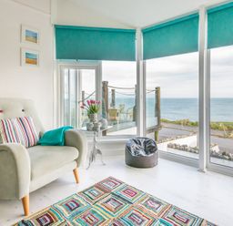 A sitting area with an armchair a small table a bean bag and large windows showing an ocean view at The View in Port Isaac