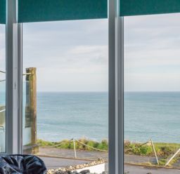A window with a view of the ocean and a balcony with wooden posts and rope at The View in Port Isaac