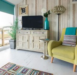 A living room with a green armchair and a striped pillow next to a wooden cabinet with a TV and a blue vase at The View in Port Isaac