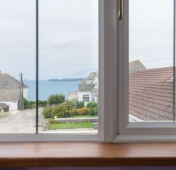 A view of houses and the sea through a window at Fairholme in Port Isaac