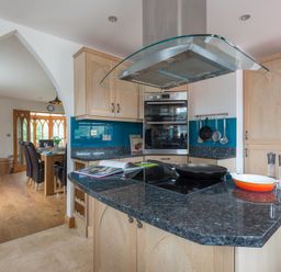 A kitchen with granite countertops and a stove next to a dining area with a wooden table and dark chairs at Fairholme in Port Isaac