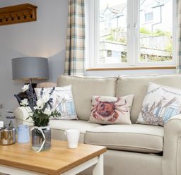 A living room with a beige sofa with cushions a wooden coffee table with a flower vase and a lamp on a side table at The Hideaway in Port Isaac