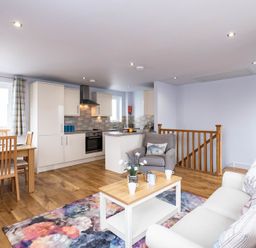 An open plan living area with a kitchen dining table sofa armchair coffee table and floral rug at The Hideaway in Port Isaac