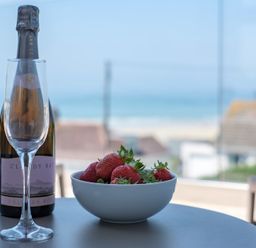 A table with a bottle of sparkling wine two empty glasses and a bowl of strawberries with a beach view at Point Break in Polzeath