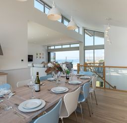 A dining table set with plates glasses and cutlery in a modern room with windows showing a sea view at Point Break in Polzeath