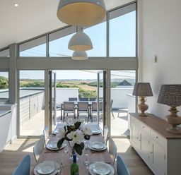 A dining area with a wooden table set for six and two patterned lamps on a sideboard at Point Break in Polzeath