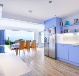 A kitchen with blue cabinets a stainless steel refrigerator and a dining area with wooden chairs at Sea Mist in Polzeath