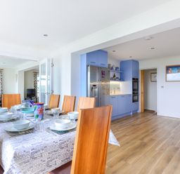 A dining table set with tableware in a kitchen with blue cabinets and wooden floor at Sea Mist Polzeath
