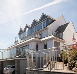 A modern multi-story house with glass balconies and metal railings and cars parked underneath