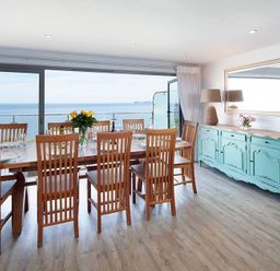 A dining room with a wooden table and chairs with a seaside view at The Crows Nest in Port Isaac