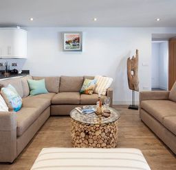 A living room with beige sofas cushions a round glass coffee table and a wooden sculpture at The Crows Nest in Port Isaac