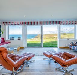A living room with leather recliner chairs glass coffee table and large windows showing a sea view at Trevan House Lundy in Polzeath