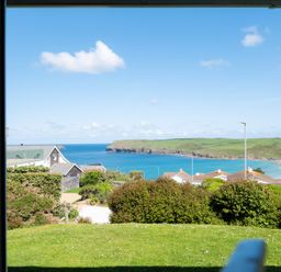 View of a coastline with houses trees and grass from inside a building at Windyhill Polzeath