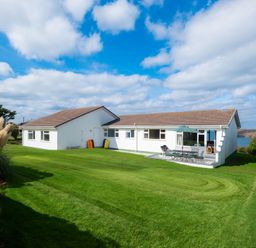 A house with a lawn and outdoor seating area at Windyhill in Polzeath