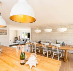 A kitchen island with a bottle of champagne and glasses overlooking a dining table with chairs and pendant lights at Seastar in Rock