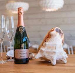 A bottle of sparkling wine with two champagne glasses and a large seashell on a wooden table at Seastar in Rock