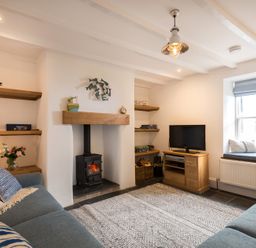 A living room with a wood stove fireplace two blue sofas wooden shelves and a TV on a cabinet at Kipper Cottage in Port Isaac
